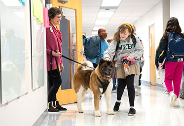 A student petting a dog in a school hallway. Links to Closely Held Business Stock